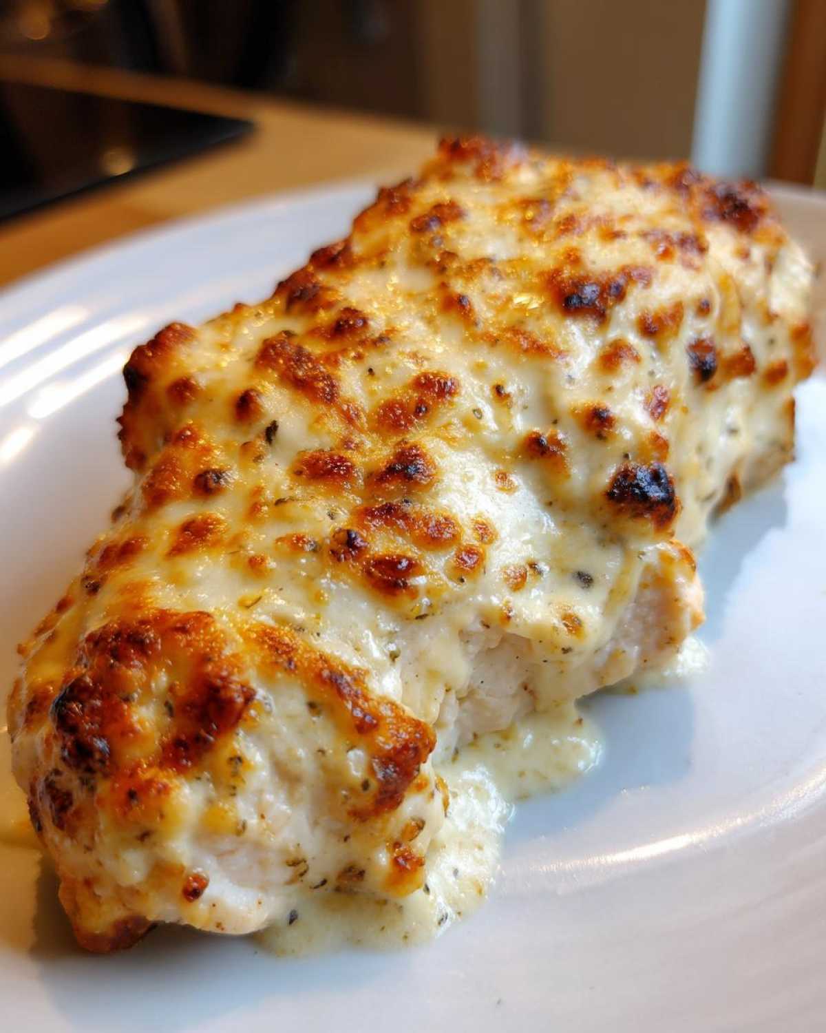A close-up of a juicy chicken breast topped with melted, golden-brown, creamy parmesan sauce, characteristic of Baked Caesar Chicken.