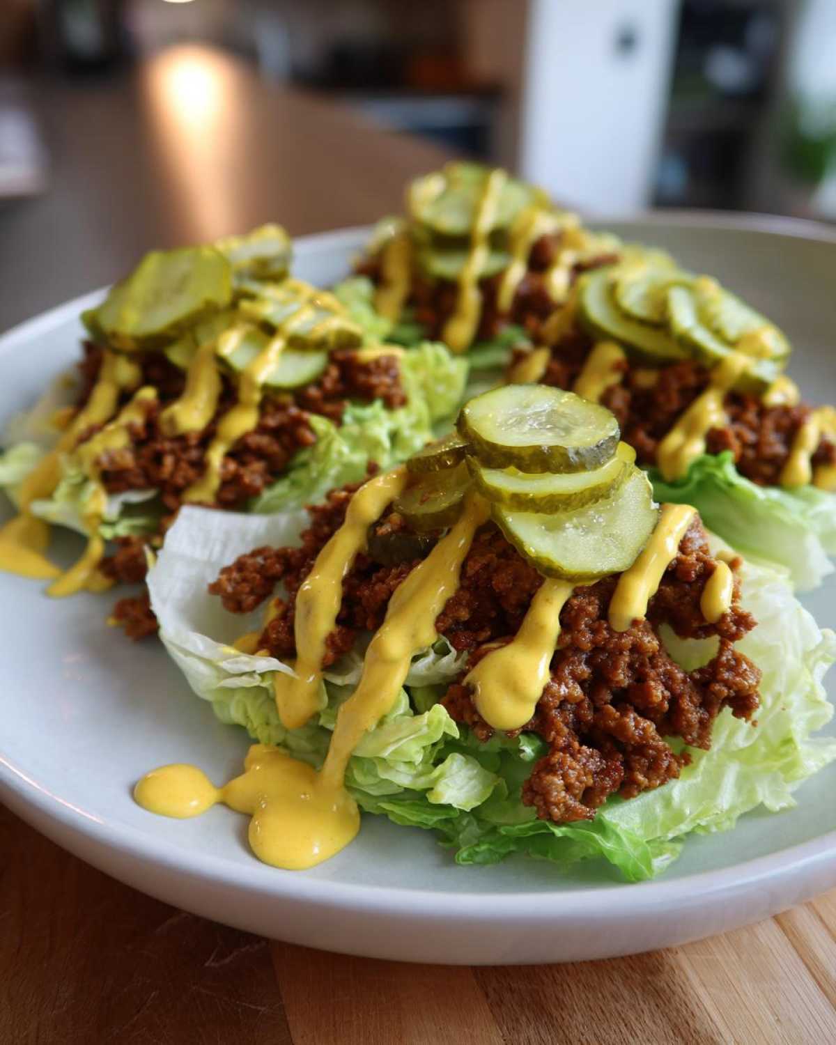 Three lettuce cups filled with seasoned ground beef, topped with pickles and a drizzle of yellow sauce, resembling a big mac salad.