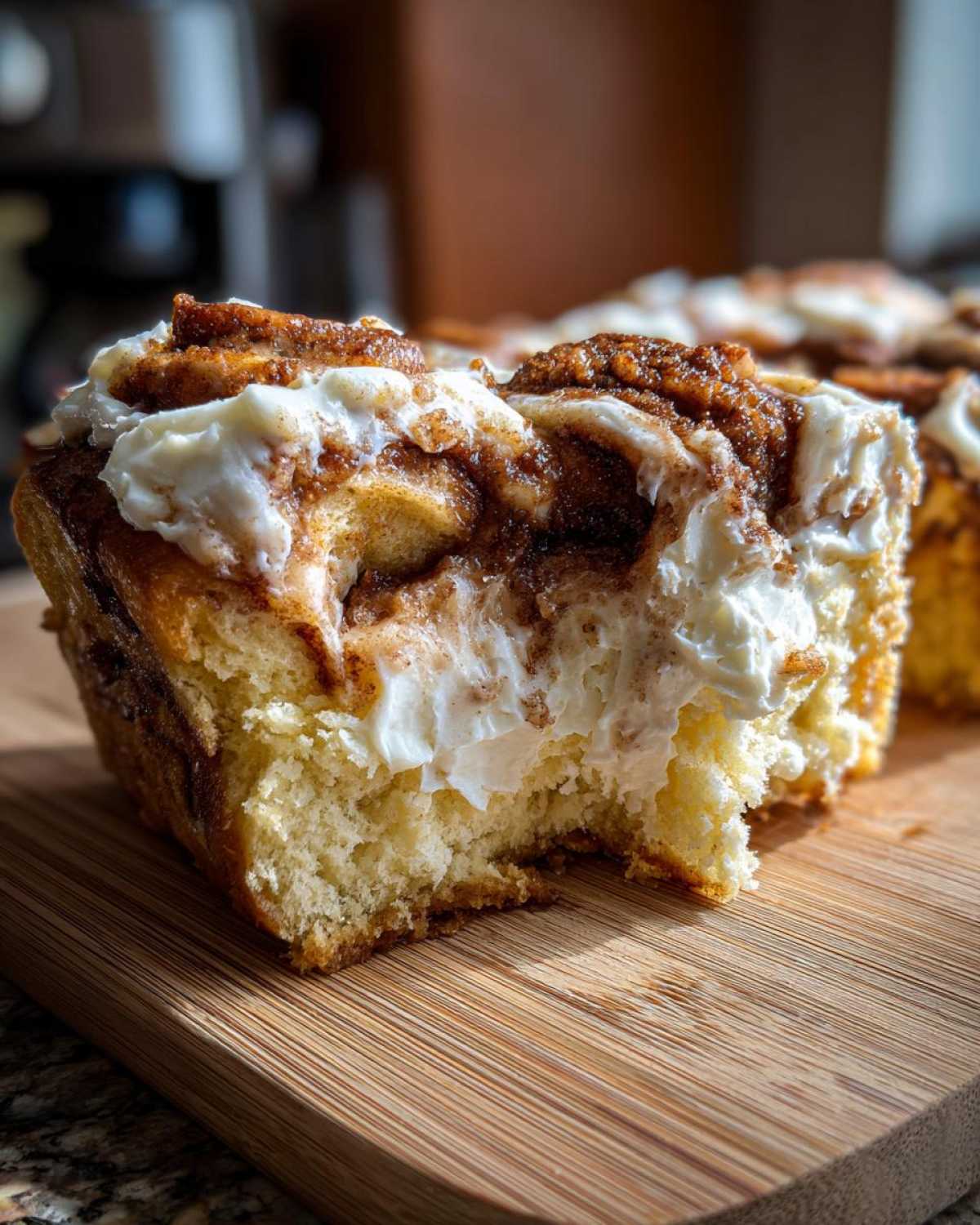 A close-up shot of a piece of moist cinnamon roll cake with a bite taken out, showing layers of cinnamon swirl and thick cream cheese frosting.