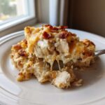 A fork lifts a cheesy, creamy scoop of Chicken Bacon Ranch Casserole topped with melted cheddar and bacon bits.