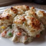A close-up of a serving of creamy chicken pot pie with biscuits topping, showing carrots and peas.