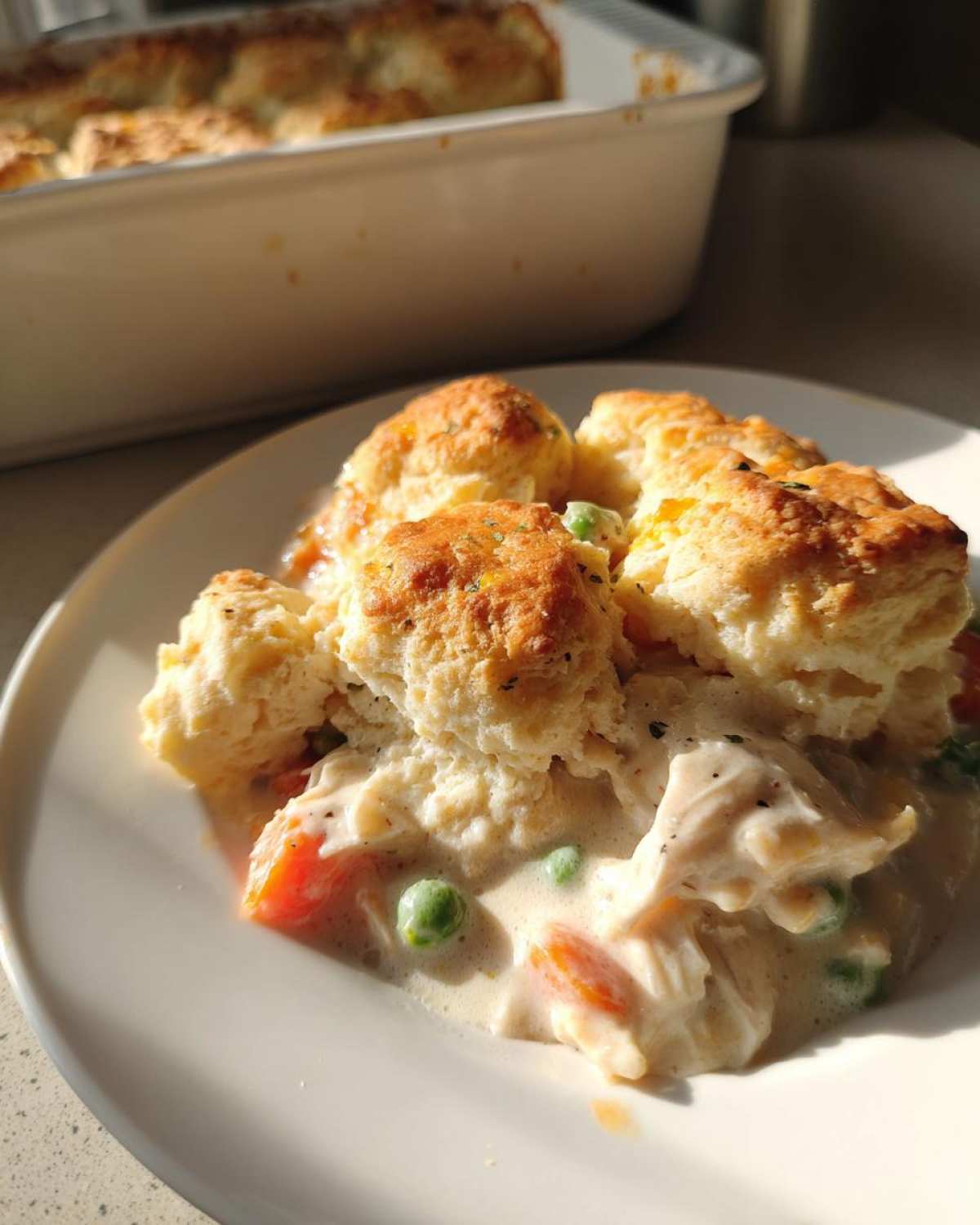 A close-up serving of creamy chicken pot pie with biscuits, featuring peas and carrots, ready to eat.