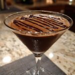 A frosty chocolate martini in a coupe glass, topped with a zigzag of dark chocolate syrup.