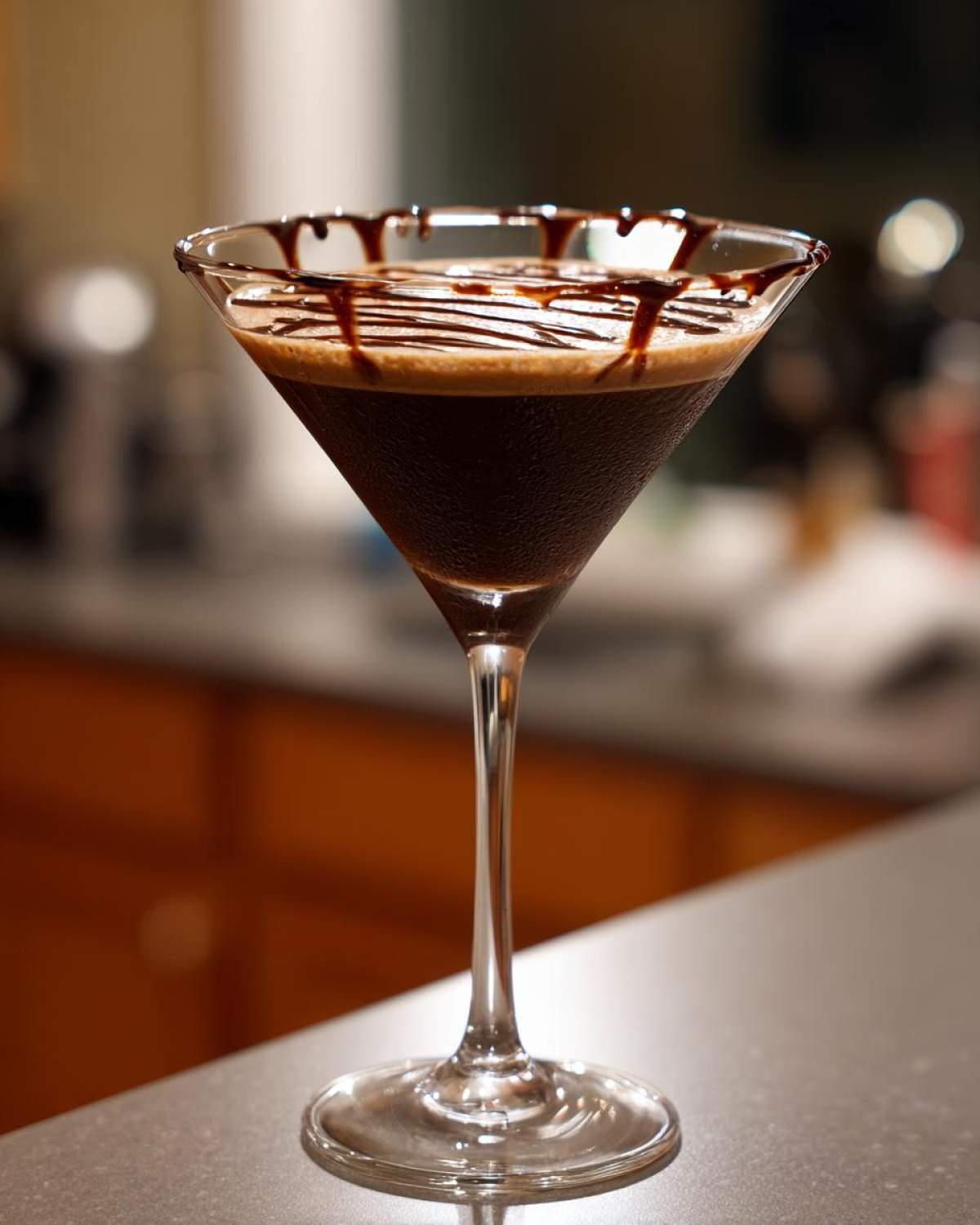 A rich, dark chocolate martini in a stemmed glass with chocolate syrup drizzled over the rim and surface.