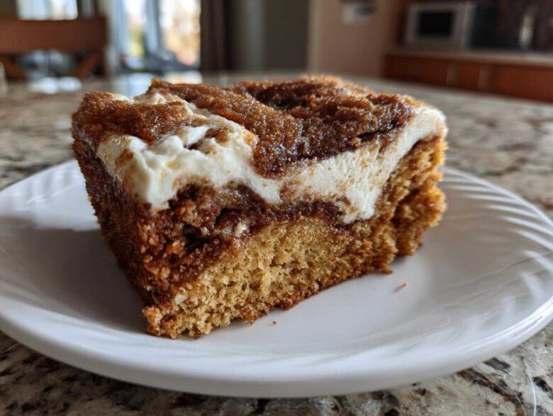 Close-up of a thick slice of cinnamon roll cake featuring a rich brown cake base, a dark cinnamon swirl, and a thick layer of white cream cheese frosting.
