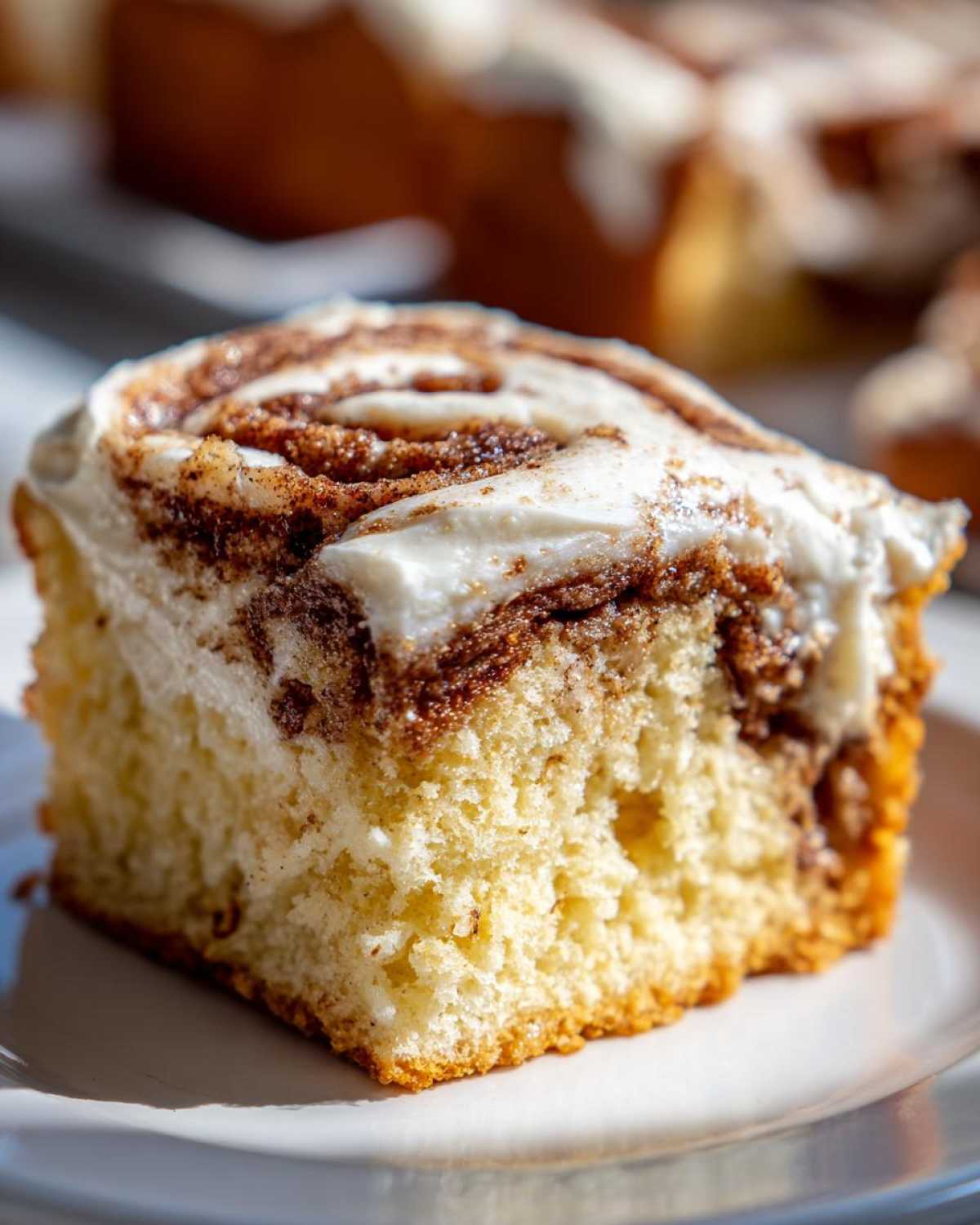 Close-up of a moist slice of cinnamon roll cake featuring a swirl of cinnamon filling and thick white frosting.
