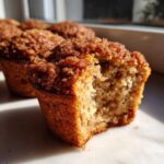 A close-up shot of a Coffee Cake Banana Bread Muffin with a bite taken out, showing the moist crumb and cinnamon streusel topping.