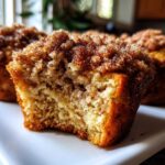 A close-up shot of a Coffee Cake Banana Bread Muffin broken open, showing the moist interior and thick cinnamon streusel topping.