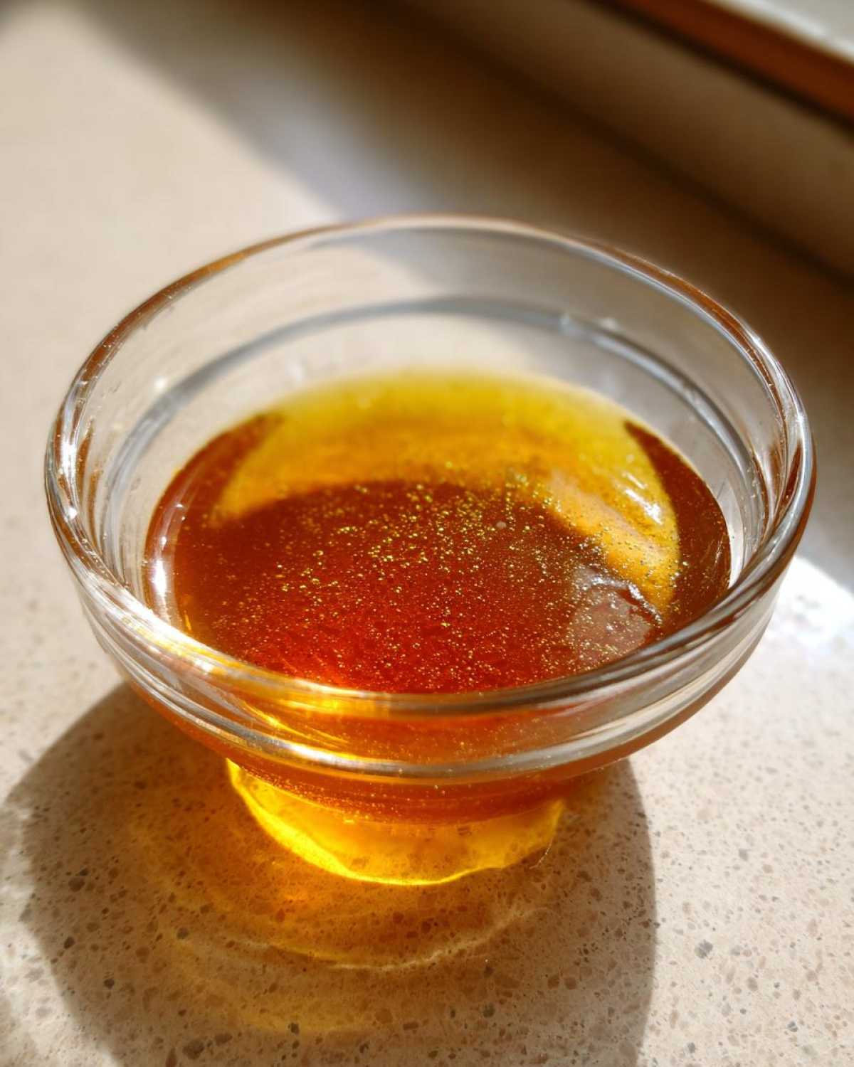 Close-up of rich, amber Copycat Apple Cider Vinaigrette settling in a small clear glass bowl.