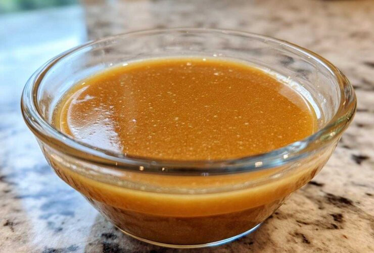 Close-up of rich, amber Copycat Apple Cider Vinaigrette dressing in a small clear glass bowl.