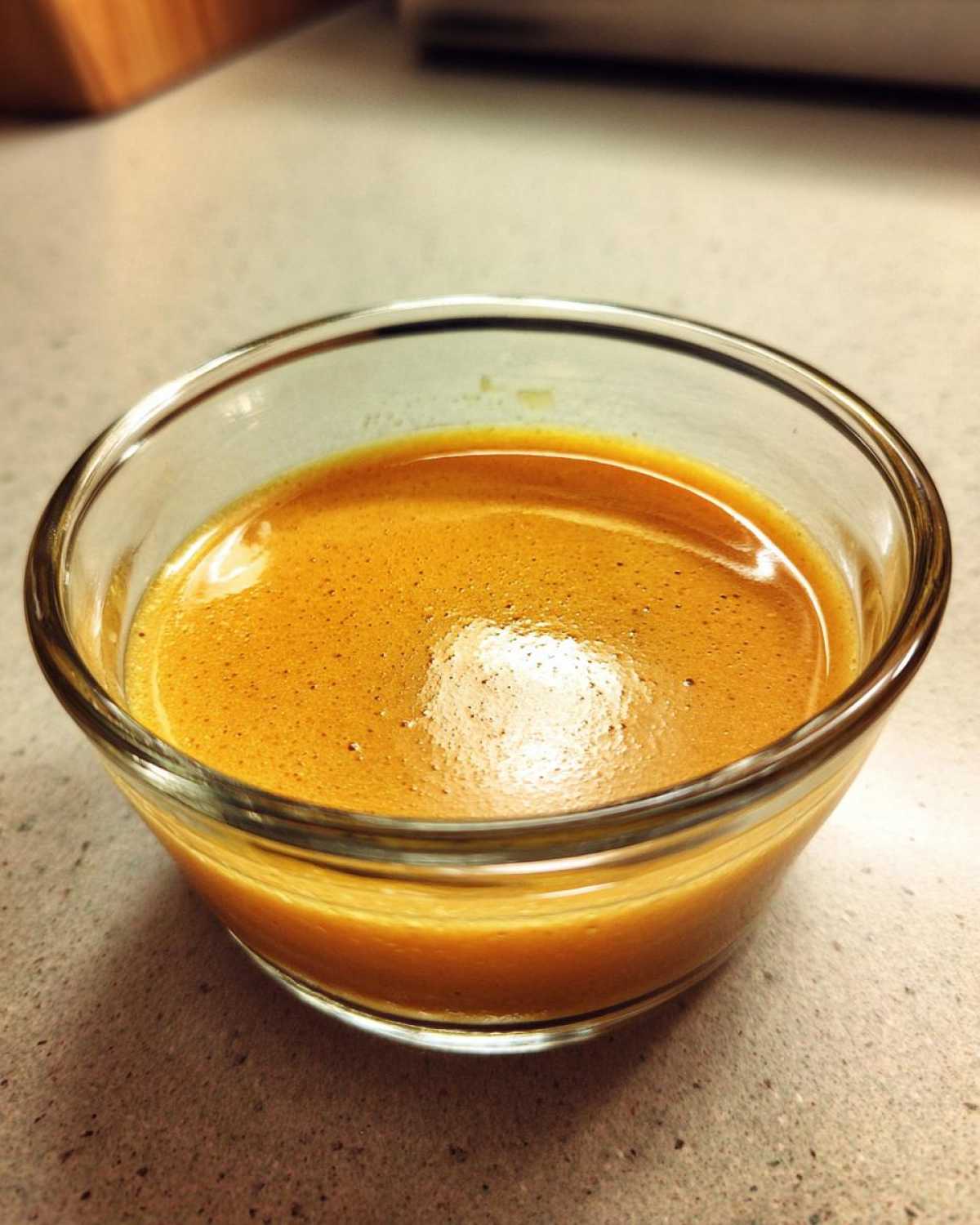 Close-up of freshly emulsified Copycat Apple Cider Vinaigrette in a small clear glass bowl.
