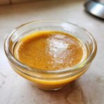 Close-up of thick, golden-brown Copycat Apple Cider Vinaigrette dressing in a small clear glass ramekin.