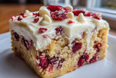 A close-up of a single square of cranberry bliss bars, featuring a dense blondie base studded with cranberries, topped with white frosting and white chocolate chips.