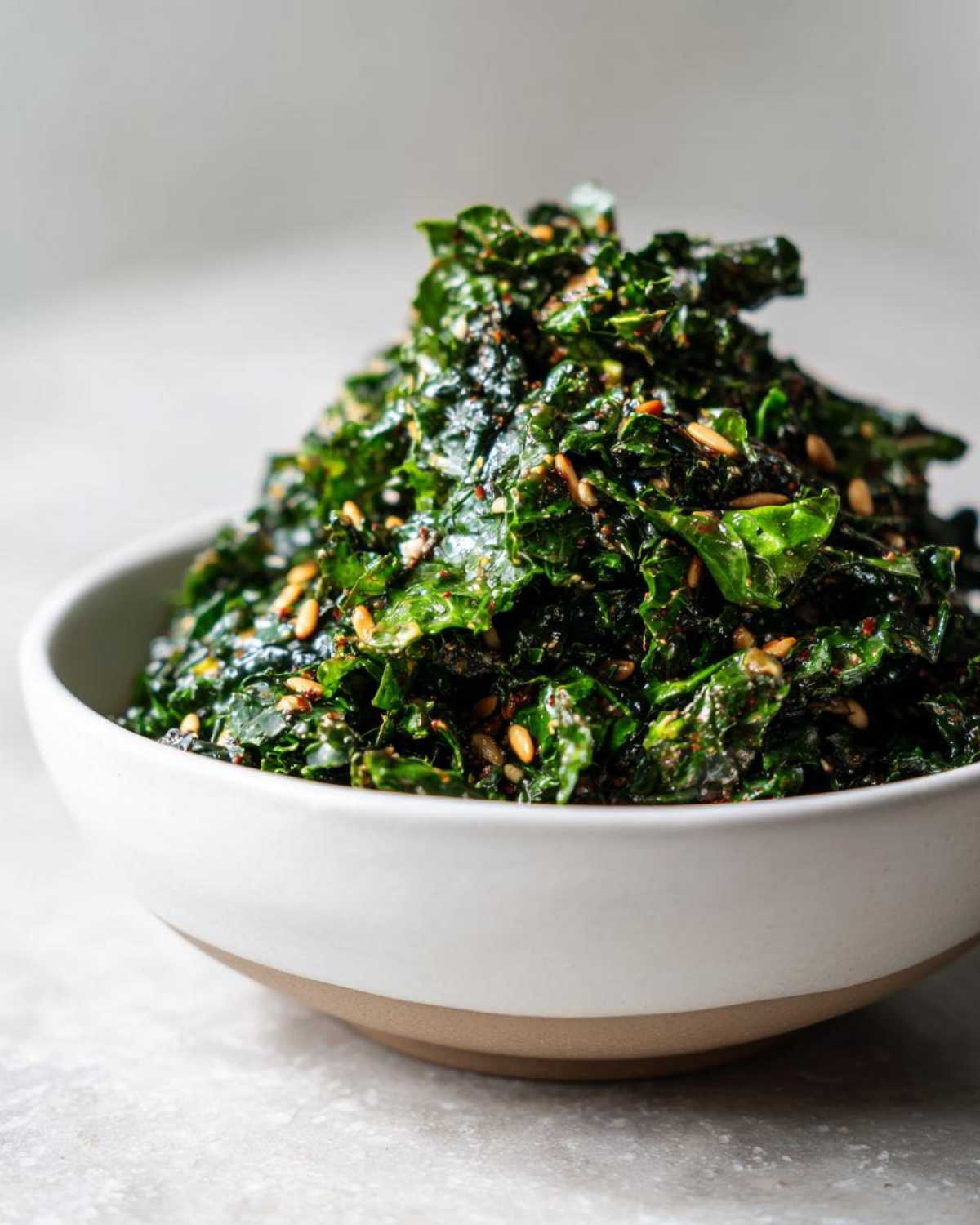 A bowl piled high with seasoned kale, resembling the Copycat Kale Crunch Salad, topped with visible seeds.