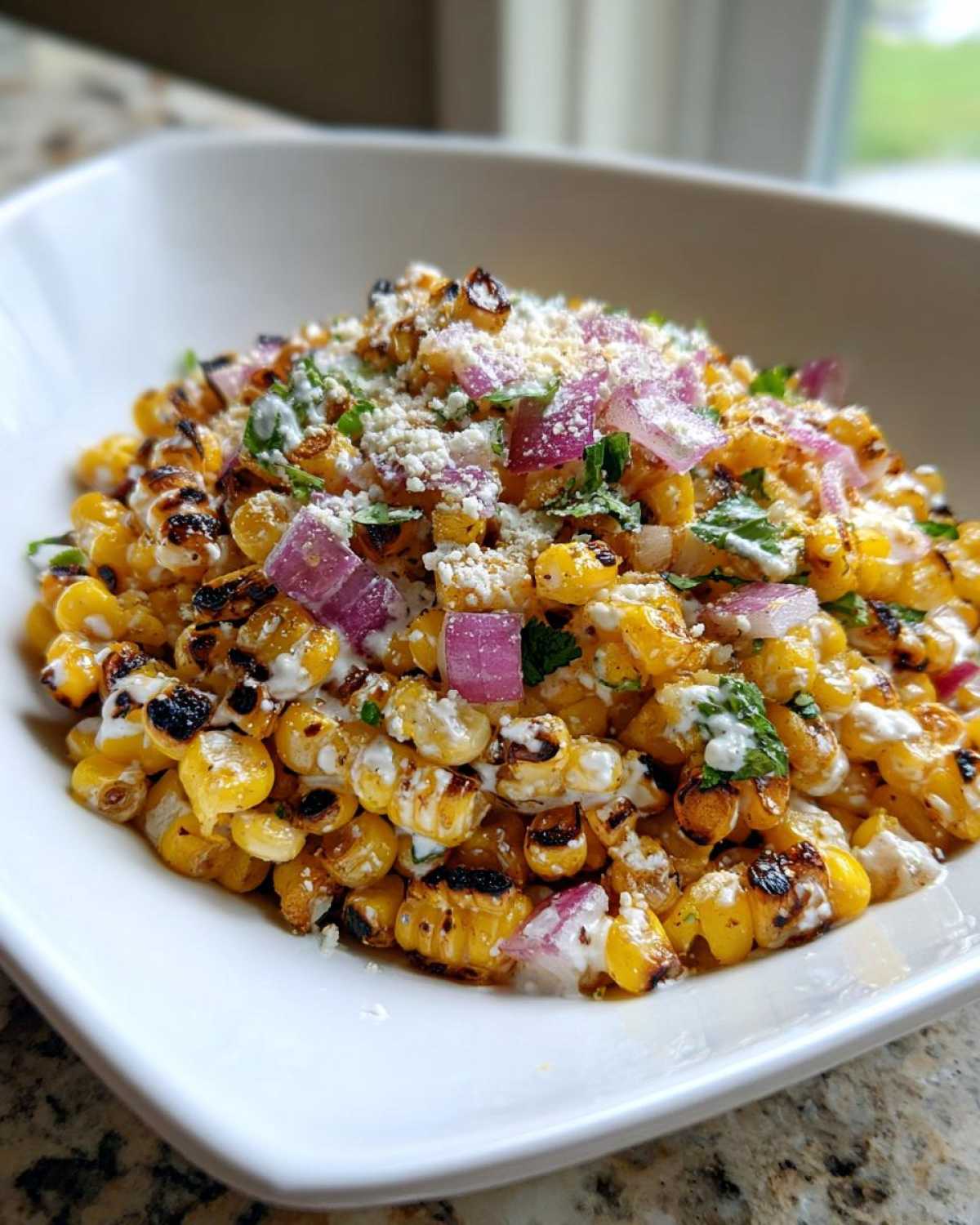 Close-up of Copycat Mexican Grill Corn Salsa featuring charred corn, red onion, cotija cheese, and cilantro in a white bowl.