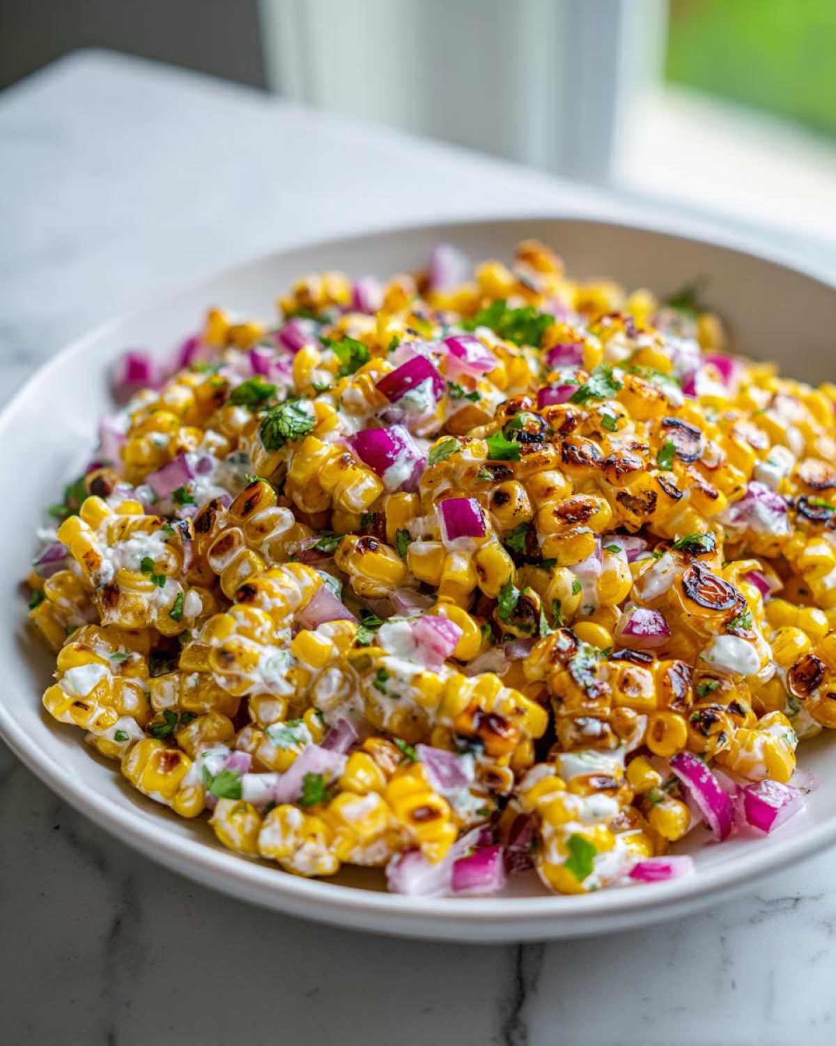 A close-up view of charred corn kernels mixed with a creamy dressing, diced red onion, and cilantro, representing the Copycat Mexican Grill Corn Salsa.