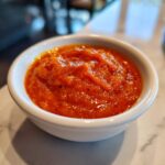 Close-up of thick, bright orange Copycat Sweet-Tangy Polynesian Dipping Sauce in a small white ramekin.