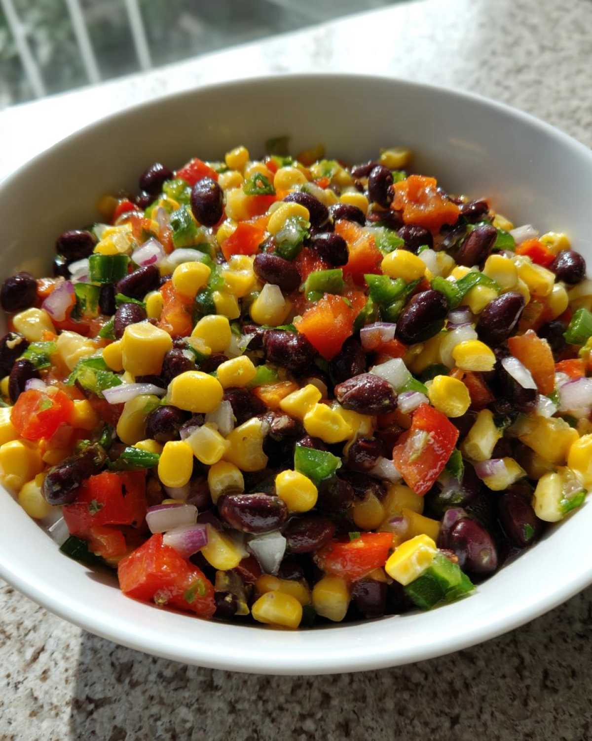 Close-up of a white bowl filled with fresh cowboy caviar recipe, featuring corn, black beans, diced tomatoes, and peppers.