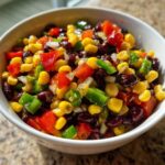 Close-up of a vibrant cowboy caviar recipe featuring black beans, corn, red peppers, green peppers, and onions in a white bowl.