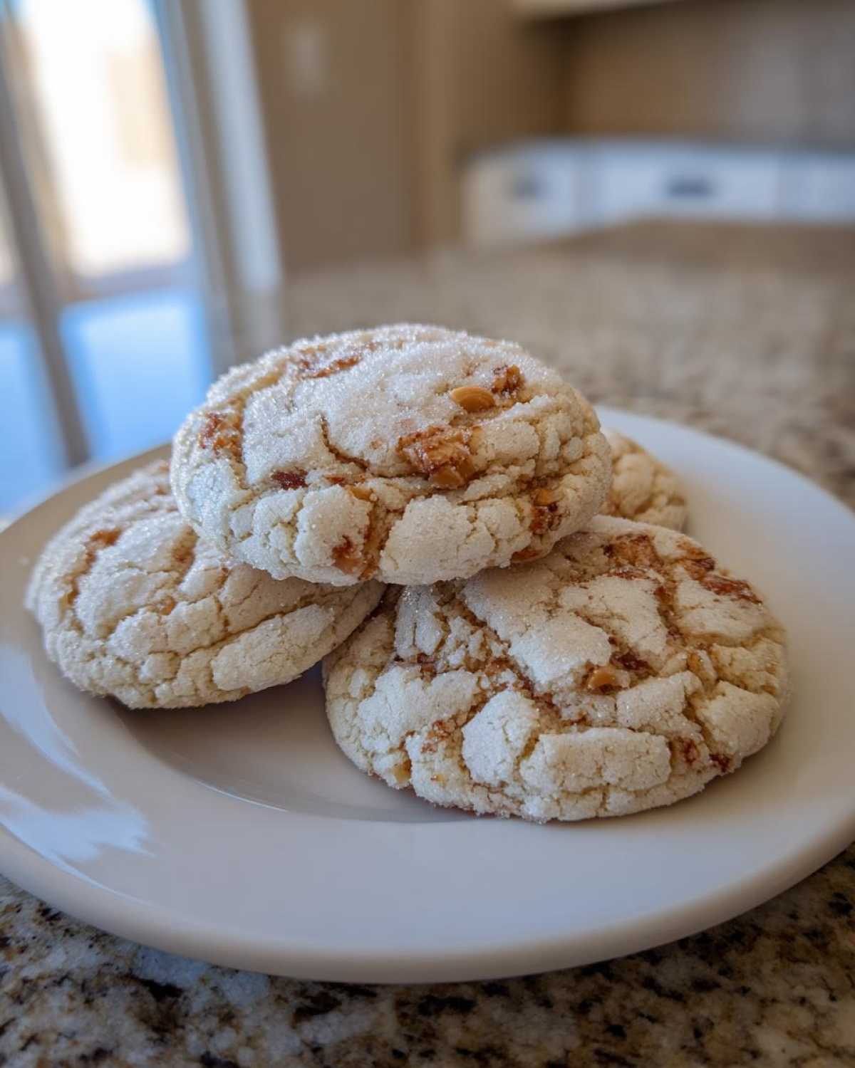 A stack of four Crackly Sugar Cookies With Rich Toffee Bits Inside resting on a white plate.