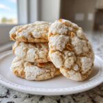 A stack of four Crackly Sugar Cookies With Rich Toffee Bits Inside, featuring a crinkled, powdered sugar top and visible toffee pieces.