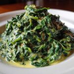 A close-up of rich, dark green creamed spinach served in a white bowl, coated in a creamy yellow sauce.