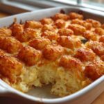 A close-up of a bubbling, golden-brown Creamy Chicken Tater Tot Casserole in a white baking dish.