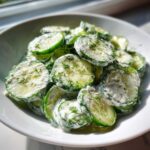 Close-up of sliced cucumbers coated in a white, creamy dressing and topped with fresh dill, showcasing the Creamy Cucumber Salad.