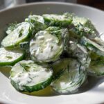 A close-up of sliced cucumbers coated in a white, creamy dressing and fresh dill, showcasing the refreshing Creamy Cucumber Salad.