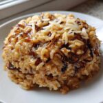 A mound of creamy French Onion Butter Rice topped with caramelized onions and shredded cheese on a white plate.