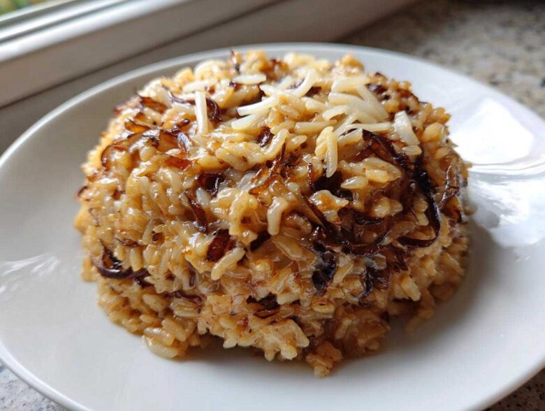 A mound of creamy French Onion Butter Rice topped with caramelized onions and shredded cheese on a white plate.