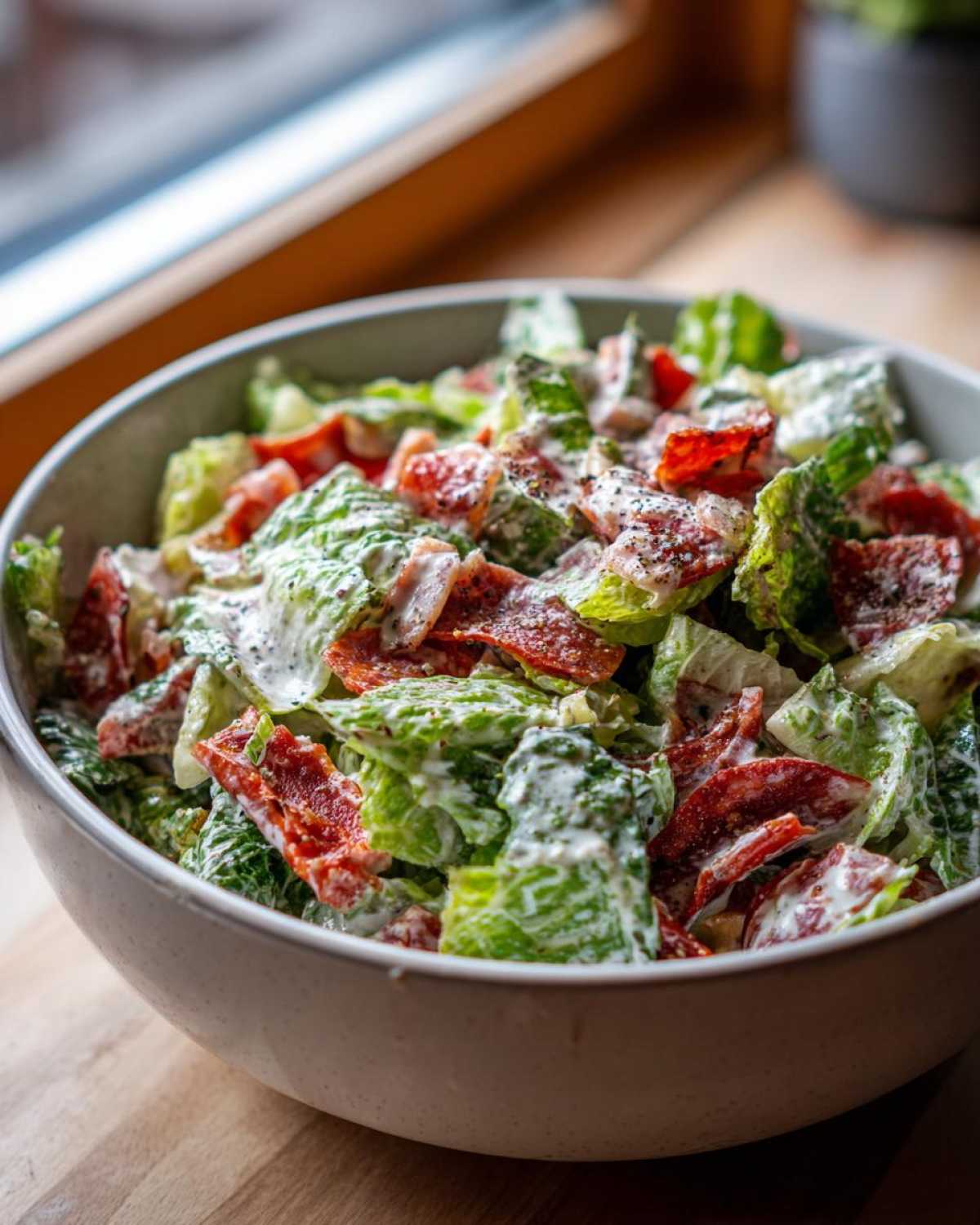 A close-up of a fresh grinder salad featuring chopped lettuce, red ingredients (likely pepperoni or tomato), and a creamy dressing, sprinkled with pepper.