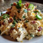 A mound of creamy jalapeno popper chicken salad topped with bacon bits, shredded cheese, and fresh jalapeno slices.
