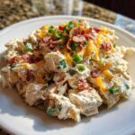 A close-up of creamy jalapeno popper chicken salad topped with shredded cheddar, bacon bits, and green onions.