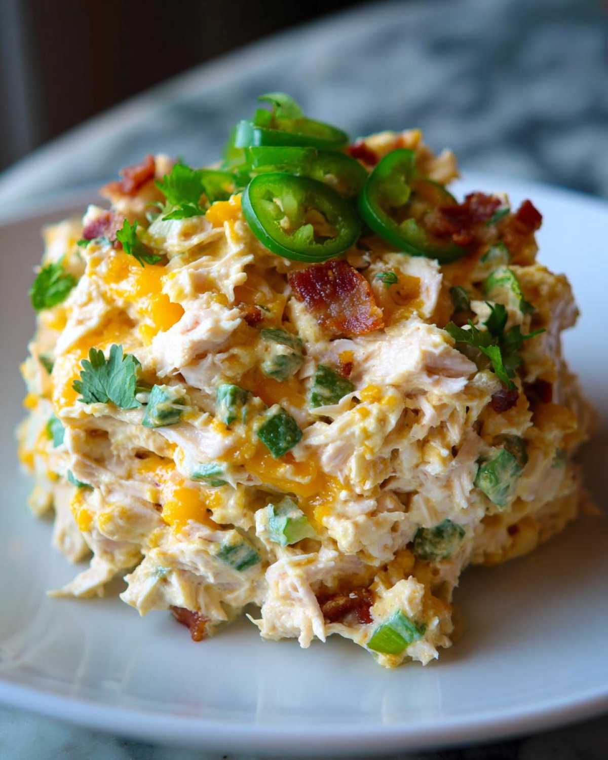 A mound of creamy jalapeno popper chicken salad topped with sliced jalapenos, bacon, and cilantro.