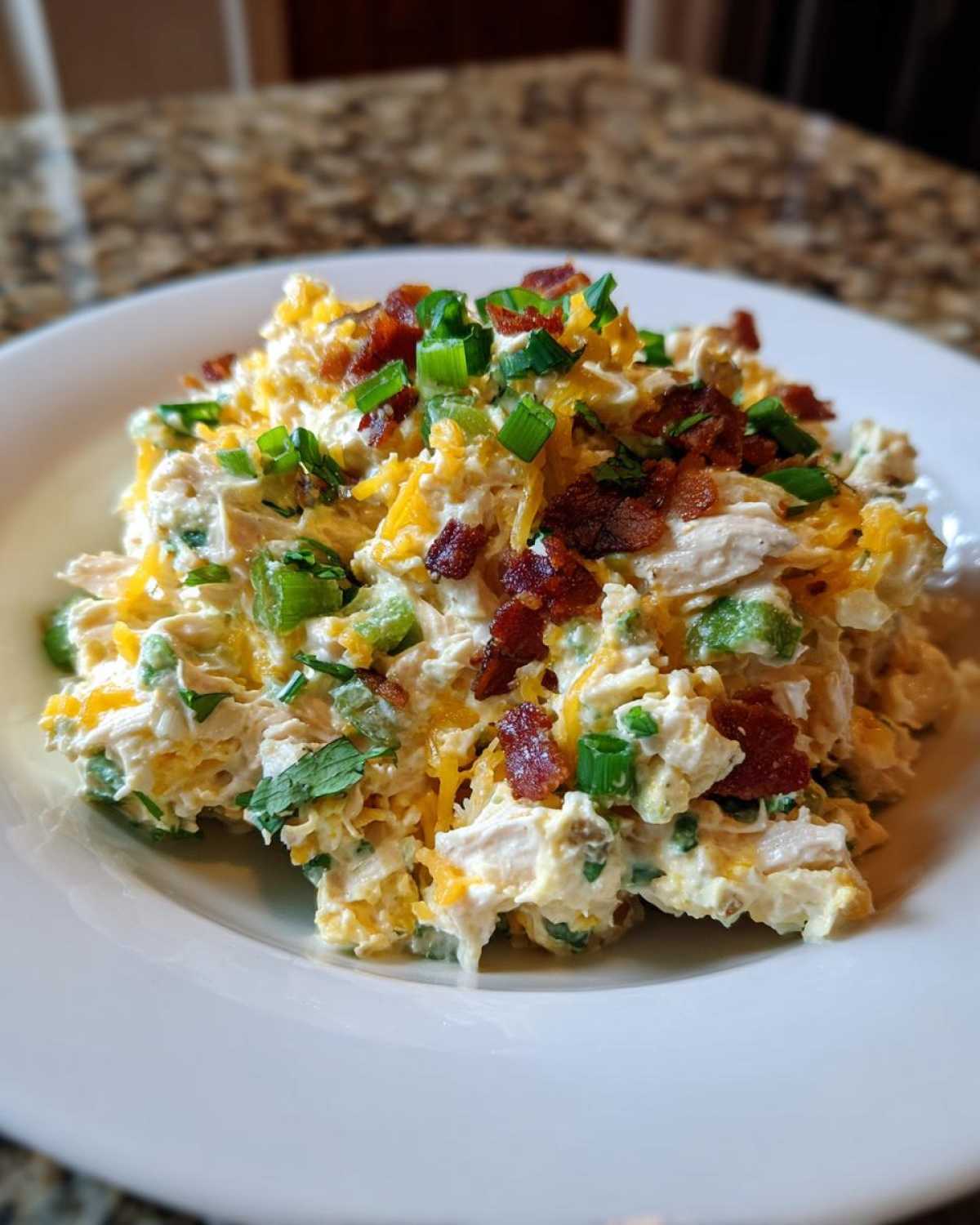 A mound of creamy jalapeno popper chicken salad topped with shredded cheddar, bacon bits, and green onions.