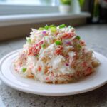 A mound of Creamy Seafood Salad with Imitation Crab, topped with chopped green onions, served on a white plate.