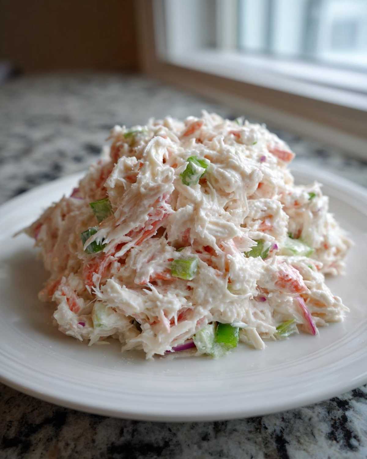 A mound of creamy seafood salad with imitation crab, celery, and red onion served on a white plate.