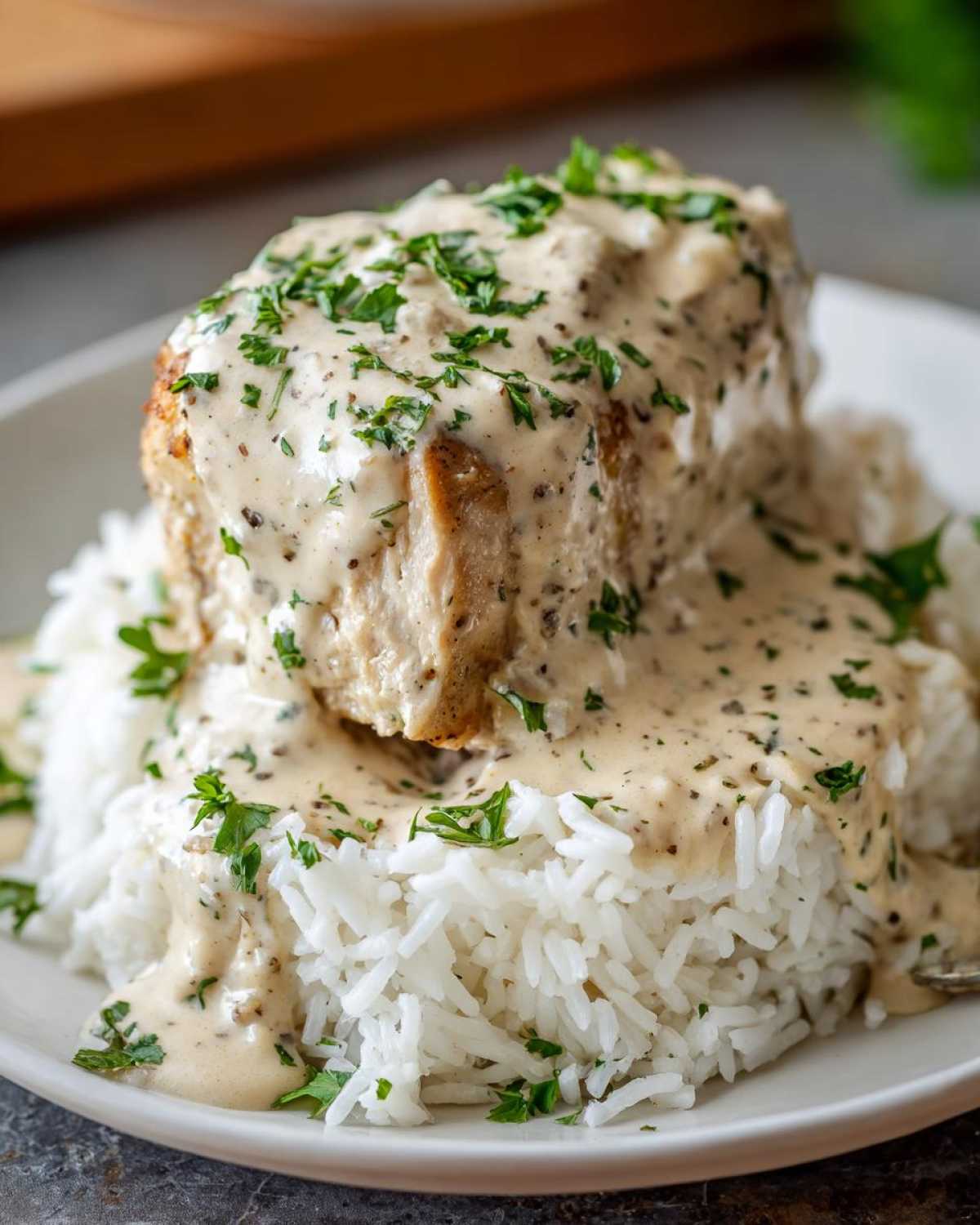 A close-up of Creamy Smothered Chicken and Rice, featuring a chicken breast covered in creamy sauce over white rice, garnished with parsley.