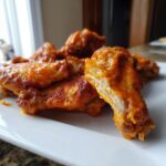Close-up of crispy, saucy buffalo wings recipe pieces piled on a white rectangular plate.