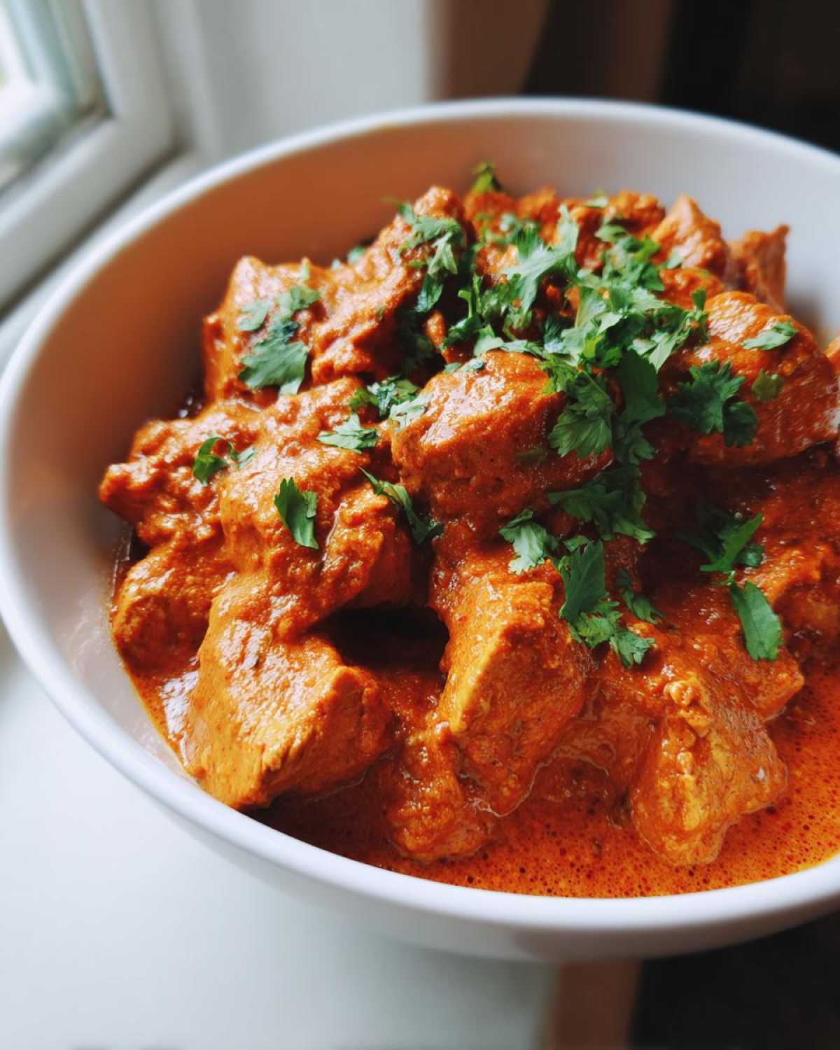 Close-up of tender chicken pieces coated in rich, orange sauce, garnished with fresh cilantro, ready to eat Crockpot Butter Chicken.