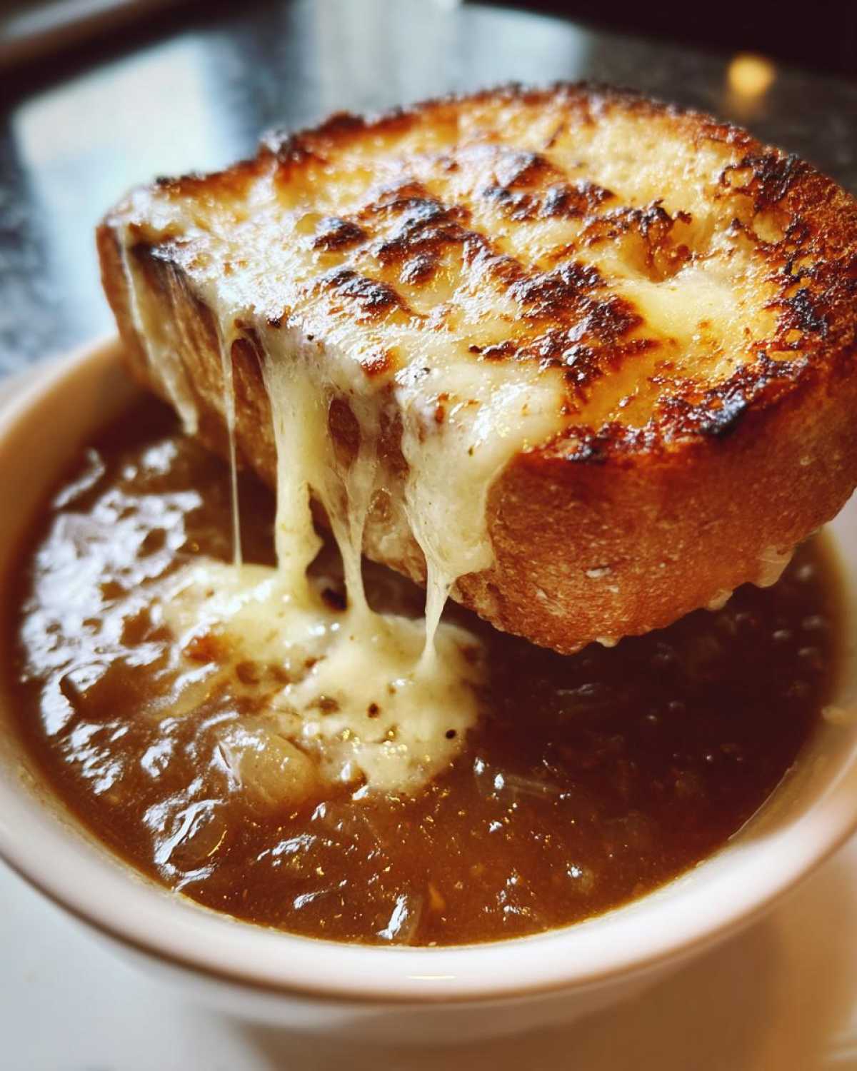 Close-up of a bowl of rich crockpot french onion soup topped with a thick slice of toasted bread covered in melted, gooey cheese.