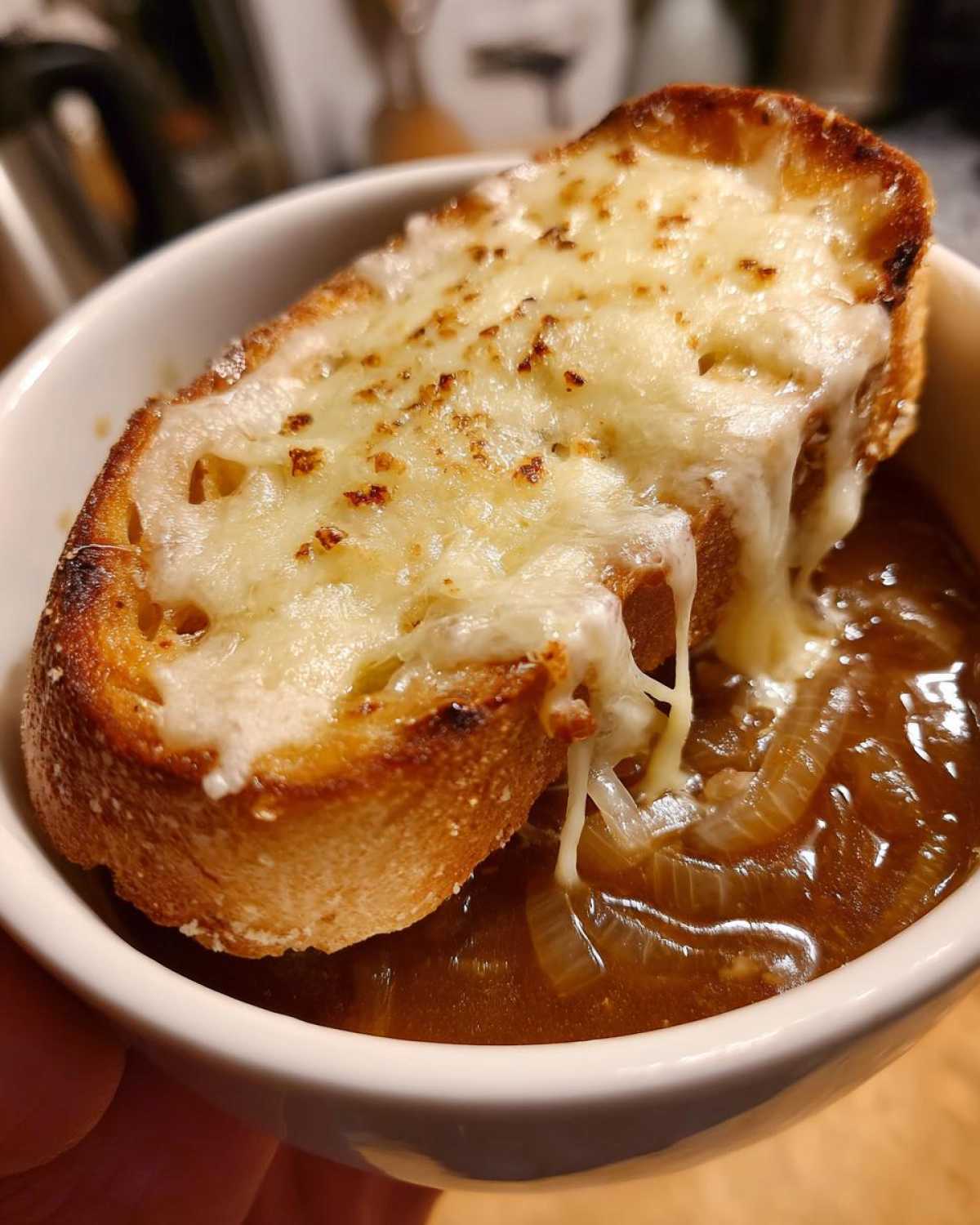 Close-up of a bowl of crockpot french onion soup topped with a thick slice of toasted bread and melted, gooey cheese.