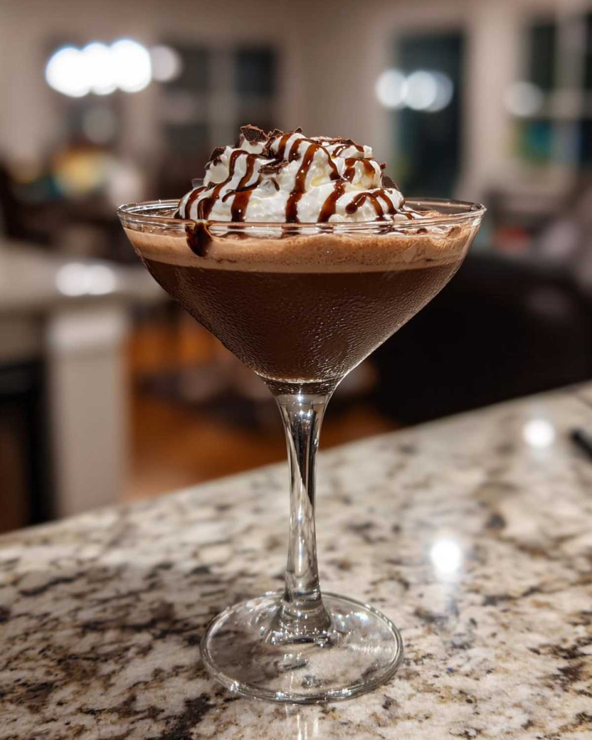 A rich chocolate martini in a coupe glass, topped with whipped cream, chocolate syrup drizzle, and shavings.