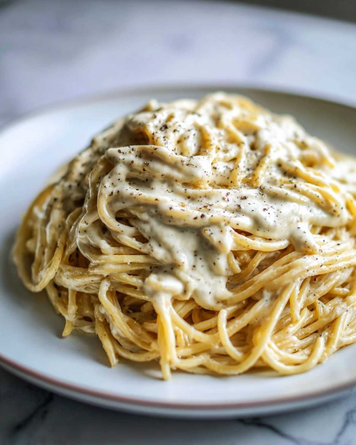 A plate of spaghetti generously coated in creamy Easy Cottage Cheese Alfredo Sauce and topped with black pepper.