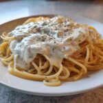 A close-up of spaghetti topped generously with creamy Easy Cottage Cheese Alfredo Sauce and cracked black pepper.