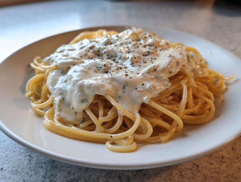 A close-up of spaghetti topped generously with creamy Easy Cottage Cheese Alfredo Sauce and cracked black pepper.