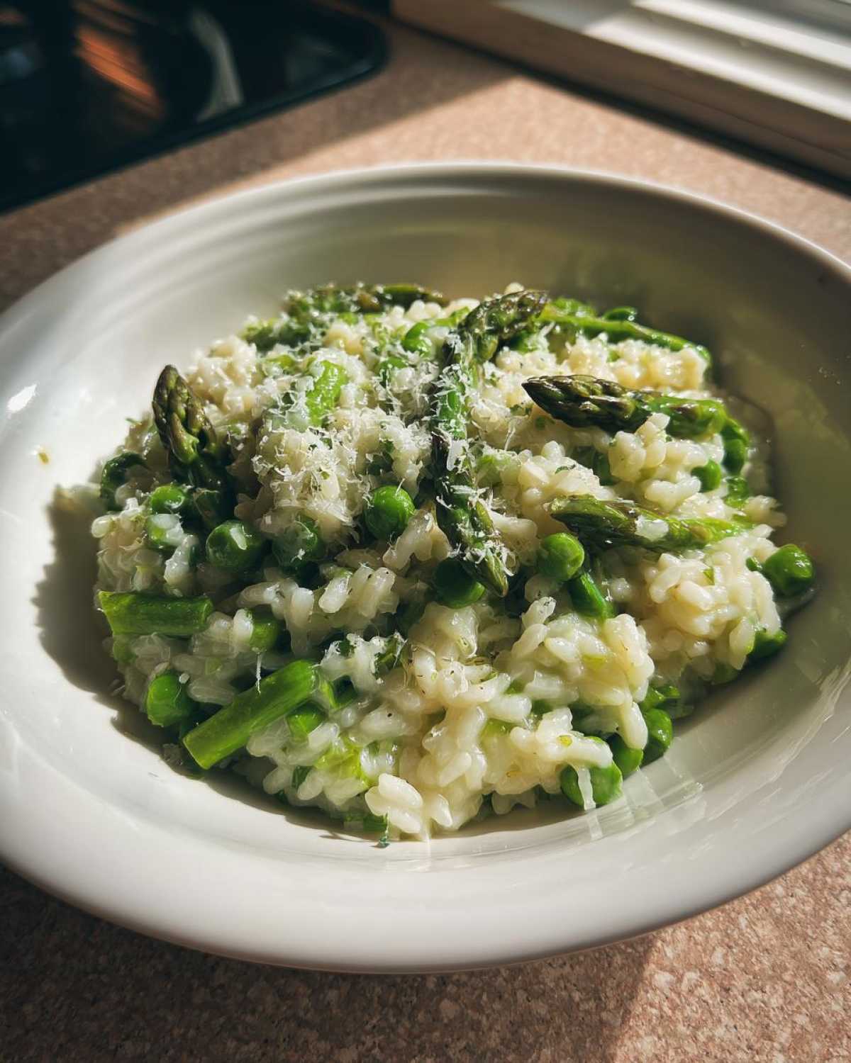 A close-up of a white bowl filled with Easy Creamy Asparagus Risotto, topped with grated Parmesan cheese.