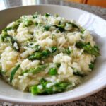 A close-up bowl of Easy Creamy Asparagus Risotto topped with shaved Parmesan cheese.
