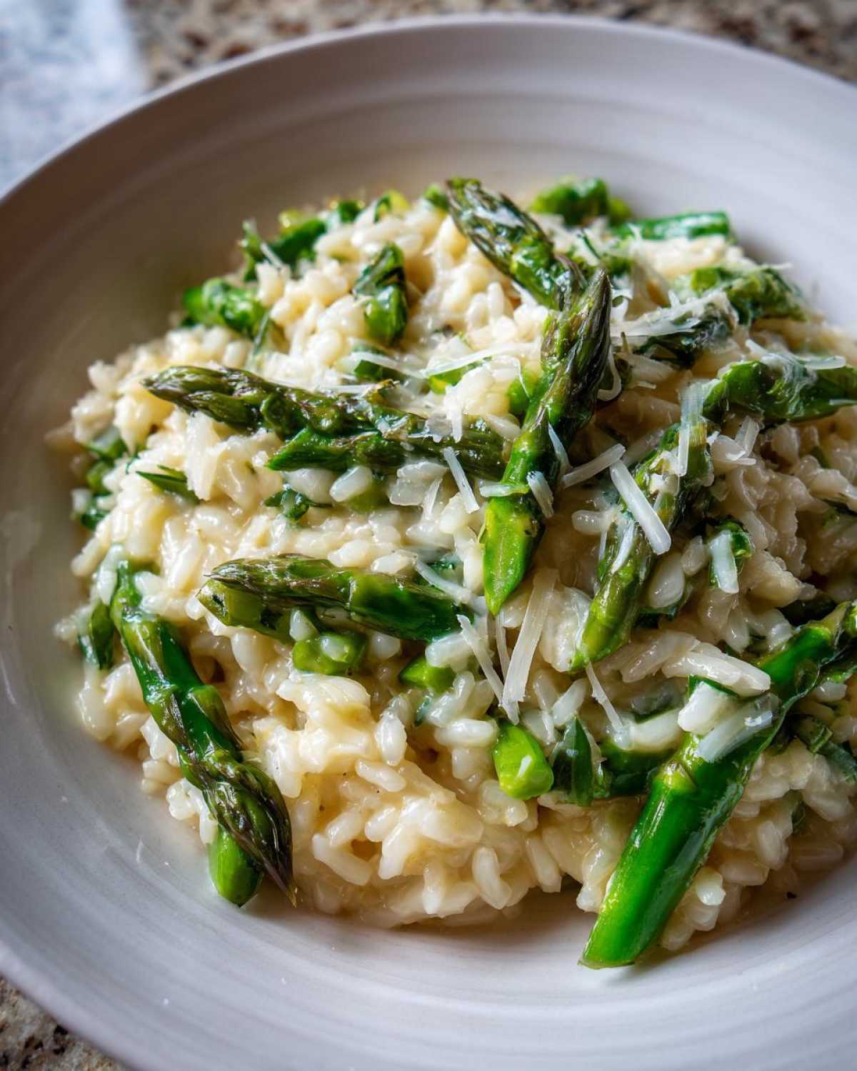 A close-up shot of Easy Creamy Asparagus Risotto topped with bright green asparagus spears and grated Parmesan cheese.